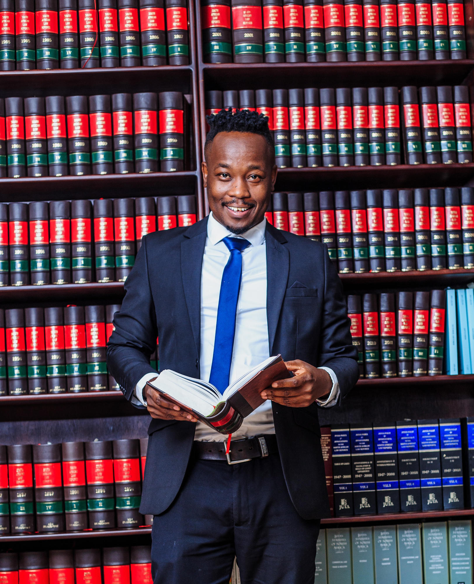William Mahesu standing in front of a legal library with an open law book